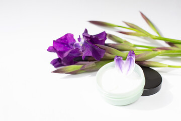 Fototapeta na wymiar Iris flowers and a jar of cream are on a white background. Natural cosmetics theme. Free space for text.