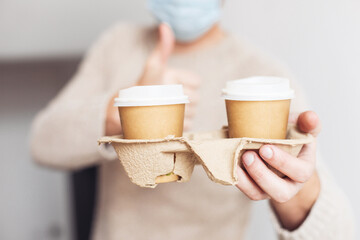 Man in a medical mask holding two takeaway paper cups in a cardboard holder 