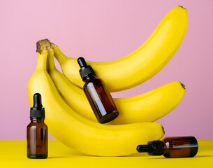 Moisturizing cosmetic oil brown glass bottles and bananas on a pink and yellow background, beauty care concept