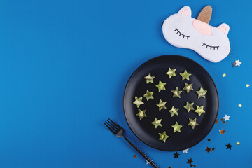 Kiwi slices in the shape of stars on a plate as a product to restore healthy sleep on a blue background. Top view with copy space
