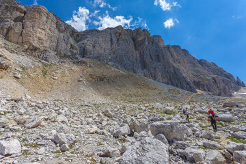 Fototapeta premium Unrecognizable trekkers walking on a hiking trail at the foots of western rocky wall of the mount Settsass, Dolomites, Italy
