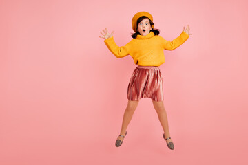 Studio shot of jumping girl in yellow sweater. Excited child dancing on pink background.