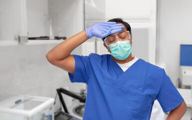 Fototapeta na wymiar healthcare, profession and medicine concept - tired indian doctor or male nurse in blue uniform and face medical mask for protection from virus disease over laboratory or hospital background