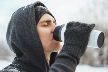 Man athlete drinking from the thermal mug during snowy winter day
