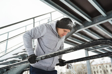 Fototapeta na wymiar Young athletic man doing dips on a parallel bars during his winter workout