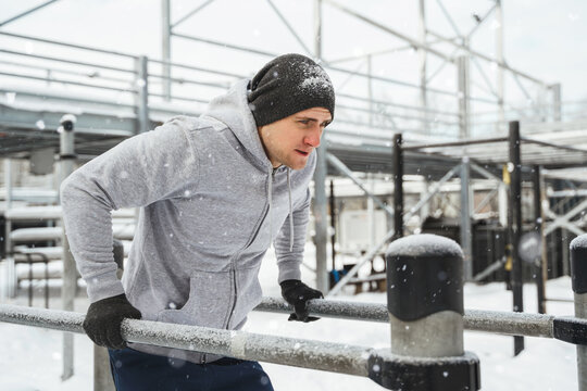 Young athletic man doing dips on a parallel bars during his winter workout