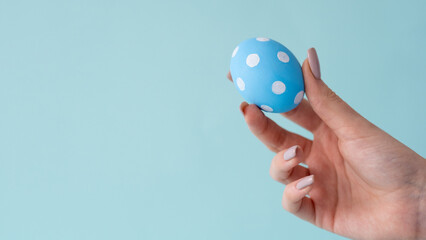 Easter art. Holiday decoration. Handmade food ornament. Spotted color egg with polka dot minimal pattern in female hand isolated on blue copy space background.