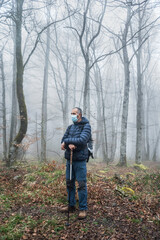Obraz premium Man hiker with mask with walking sticks in a forest. Autumn or winter landscape with mist. Trees on the background.