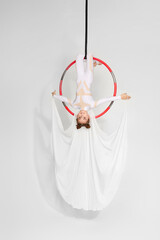 Little acrobat girl shows an acrobatic performance on an aerial hoop
