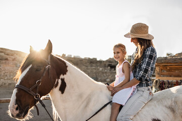 Happy mother and daughter riding a horse at sunset - Main focus on woman