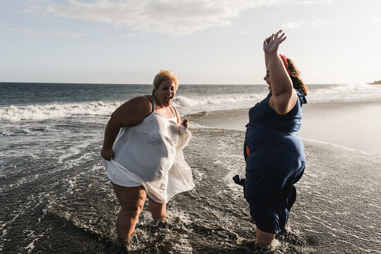 Curvy women dancing on the beach having fun during summer vacation - Main focus on left woman face