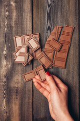 female hand and broken bar of chocolate on wooden table portrait