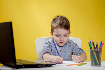 Happy Child using digital laptop doing homework on yellow background. Social Distancing, E-learning online education