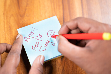 POV shot of hands writing April fools day on sticky notes, concept of preparing for prank or fools day celebration.