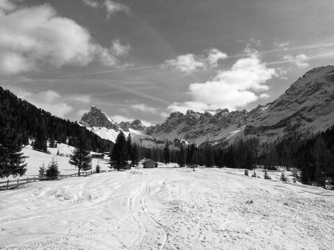 Panorama di montagna - Valle innevata con baita di montagna e dolomiti di sfondo - Nuvole bianche in cielo 