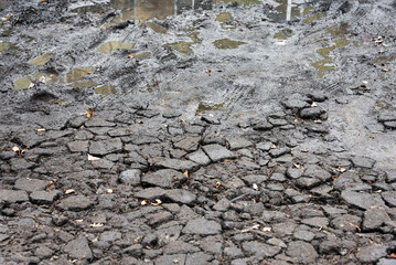 Broken asphalt with dirt. Bad bumpy road with potholes, destroyed asphalt and puddles. Water pits on broken asphalt. Spring and autumn problems for drivers.