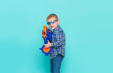 Portrait of kid playing with plastic gun, isolated on blue background. Beautiful caucasian teenager...