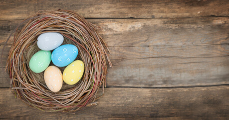 Color Easter eggs in bird's nest on wooden background - top view	