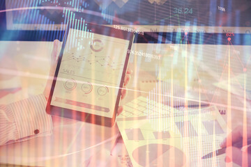 Double exposure of man's hands holding and using a digital device and forex graph drawing. Financial market concept.