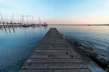 Fototapeta na wymiar Pier on Lake Garda. Lake Garda at sunset, wooden jetty. BArche on the horizon in the lake