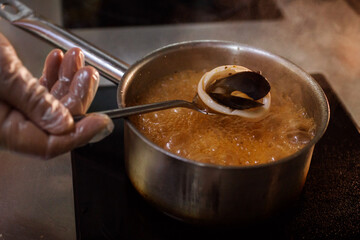 Chef in gloves is showing mussel in shel and squid on spoon above boiling broth.
