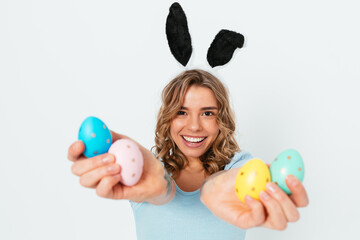 Fototapeta na wymiar Happy young woman in ears of Easter bunny showing colored eggs