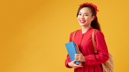 Pretty young girl in casual clothes with backpack posing isolated on yellow background. Education in high school university college concept. Hold books
