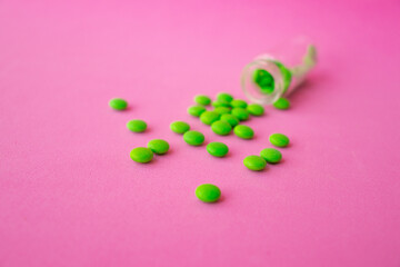a glass ampoule is lying on the table a pile of green pills close up on a pink background