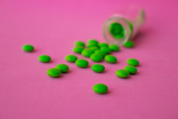 a glass ampoule is lying on the table a pile of green pills close up on a pink background
