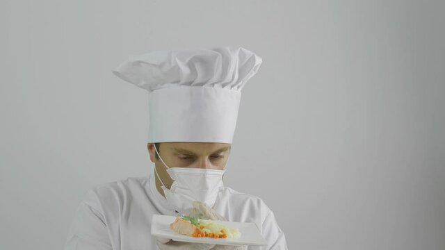 The chef wearing white cap and uniform, take off protective mask and smell plate