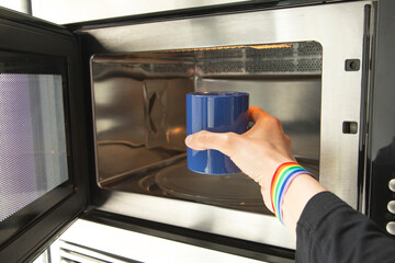 Hand with rainbow bracelet putting a blue bowl in the microwave