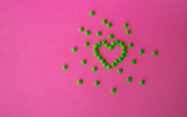 heart of green pills on a pink background, heart-shaped pills laid out on a table close-up