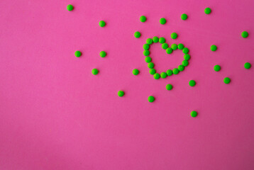 heart of green pills on a pink background, heart-shaped pills laid out on a table close-up