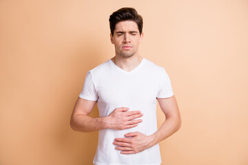 Photo of young man closed eyes holding hands on belly feels bad isolated on beige color background
