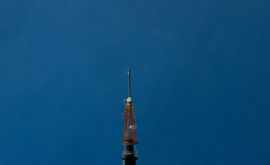The needle of a syringe with a vaccine close-up on a blue background