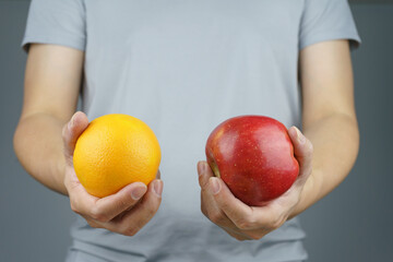 Male holding the apple in one hand and orange in another hand. It is a vegetarian and vegan food...