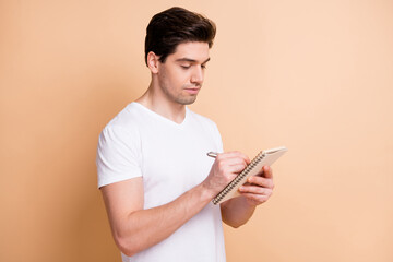 Photo of handsome young guy writing notes arm holding textbook isolated on beige color background