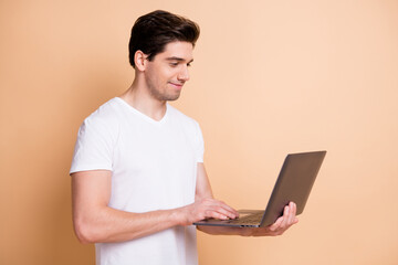 Photo of positive young guy hold use netbook typing message look screen isolated on beige color background