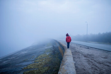 Girl walking alone along road in spring foggy day, uncertainty and hope concept, lifestyle outdoor....