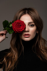 Portrait of a beautiful girl with a flower near the eyes. Red Rose. Black clothes.