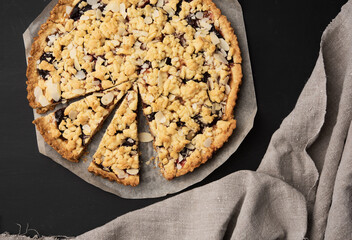 baked round crumble pie with plum cut into pieces on a black background