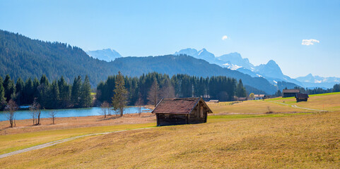 Naklejka premium pasture with wooden hay hut, lake Geroldsee and Wetterstein mountains in spring