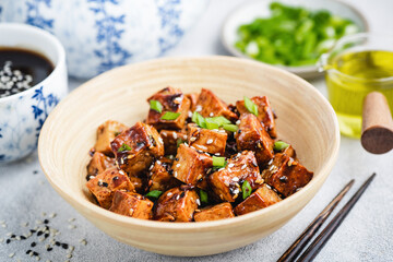 Vegan fried teriyaki tofu with scallions and sesame seeds in bamboo bowl. Asian cuisine food