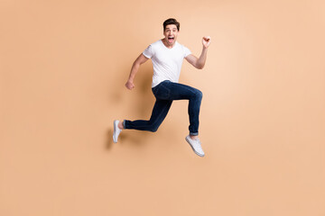 Fototapeta na wymiar Full size profile photo of hooray brunet man jump run yell wear t-shirt jeans sneakers isolated on beige background