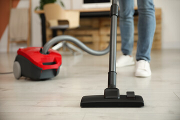 Young man using vacuum cleaner at home, closeup
