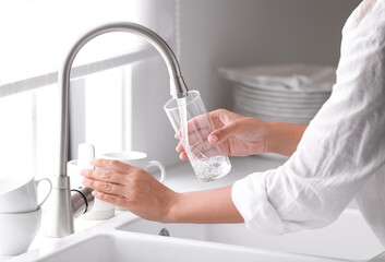 Woman pouring water into glass in kitchen, closeup