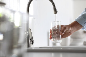 Man pouring water into glass in kitchen, closeup