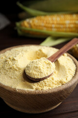 Corn flour in bowl and fresh cobs on wooden table
