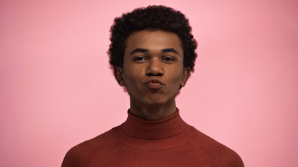 Obraz premium curly african american teenage boy in turtleneck sweater pouting lips isolated on pink