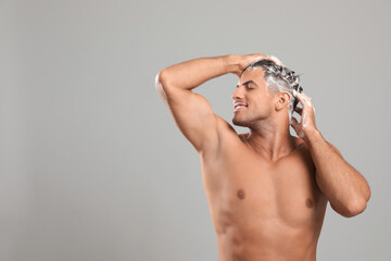 Handsome man washing hair on grey background, space for text